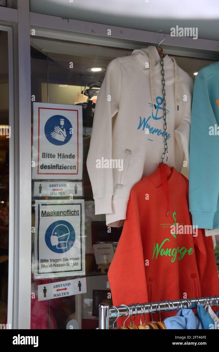 Wangerooge, Germany. 21st May, 2021. The signs next to the entrance door of  a clothing store indicate that masks are mandatory in the store and that  hands must be disinfected. Tourism in