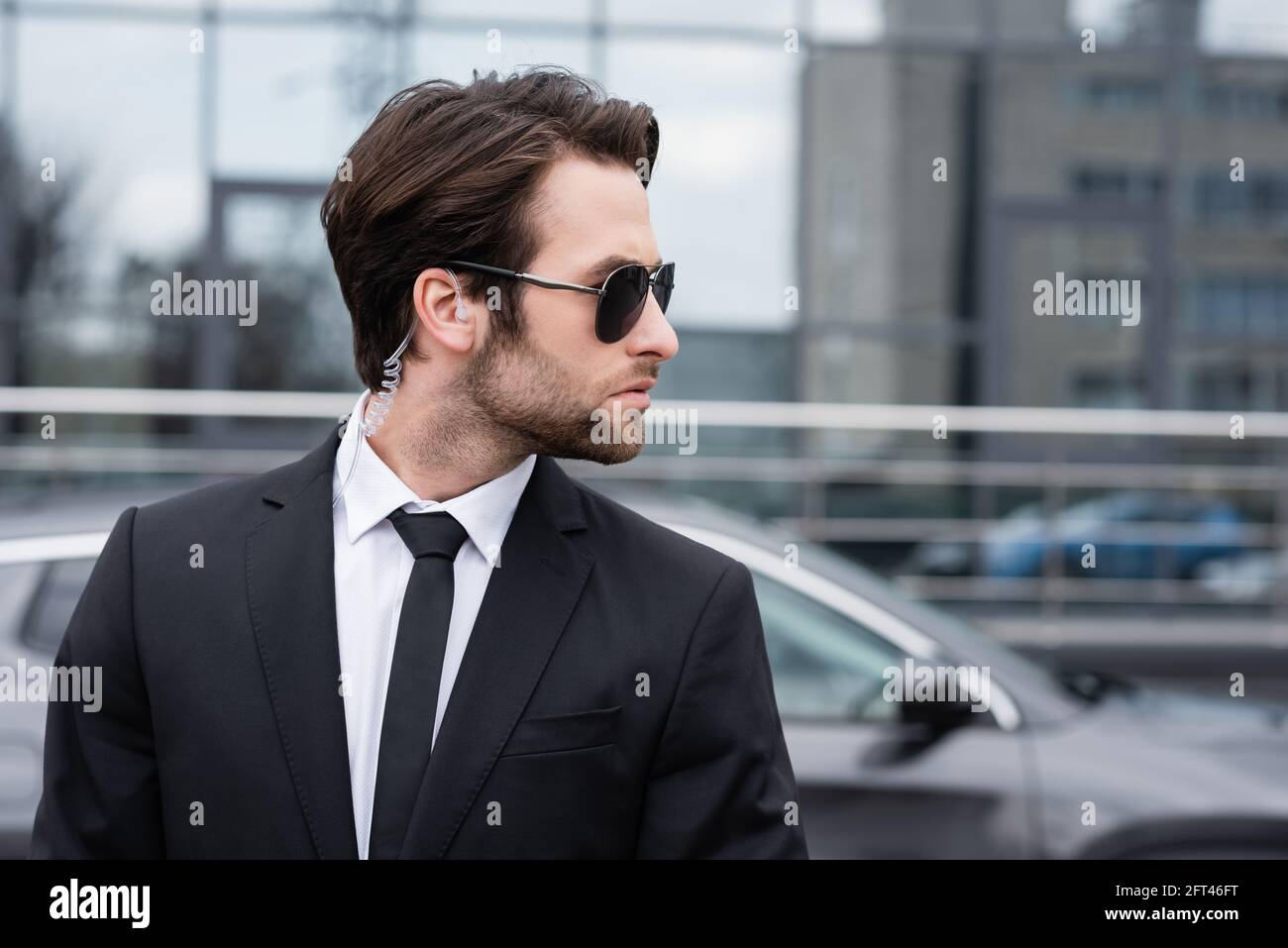 side view of bearded bodyguard in suit and sunglasses with security ...