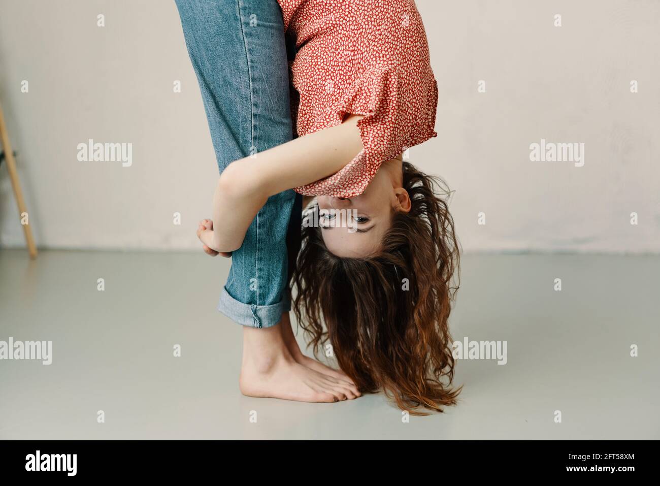 Supple young woman bending forwards to hug her legs as she playfully peeks at the camera during a yoga workout at home in a health and fitness concept Stock Photo