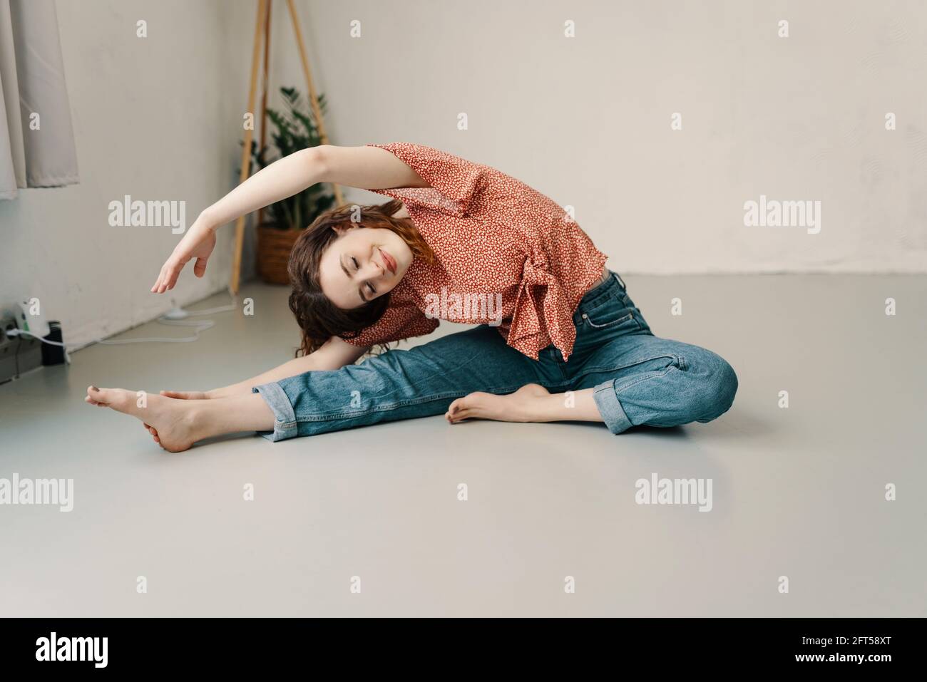 Young woma enjoying a relaxing yoga workout on the floor at home doing a graceful side stretch with eyes closed and a smile of pleasure in a health an Stock Photo