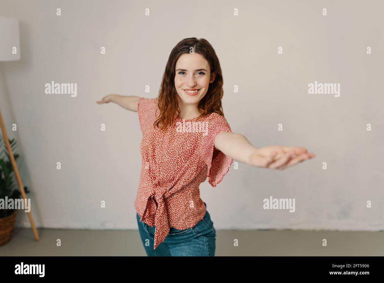Graceful happy young woman doing yoga exercises posing with outstretched arms looking at the camera with a lovely friendly smile with copyspace in a h Stock Photo