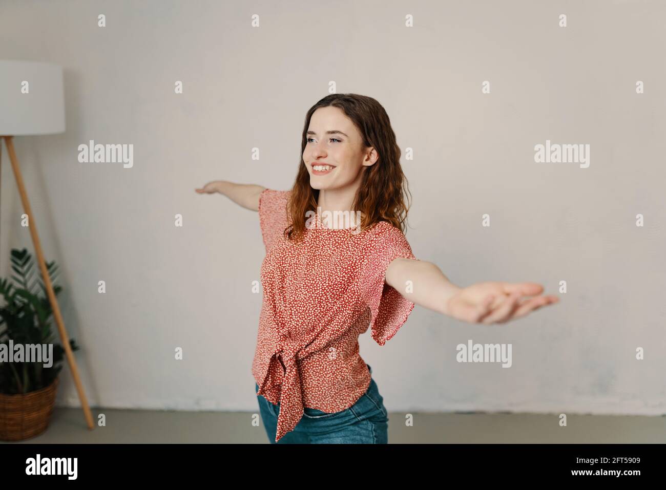 Happy young woman practicing yoga indoors with outstretched arms as she faces towards a window with a smile of pleasure in a health and fitness concep Stock Photo