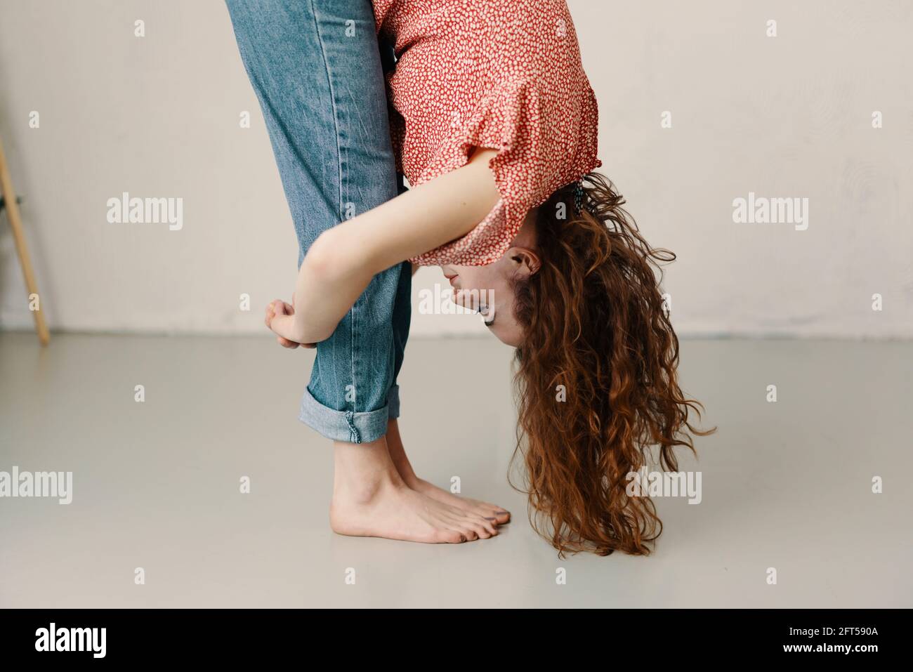 Young redhead woman bending forwards doing stretch exercises with her long hair falling forward in a close up cropped side view in a health and fitnes Stock Photo