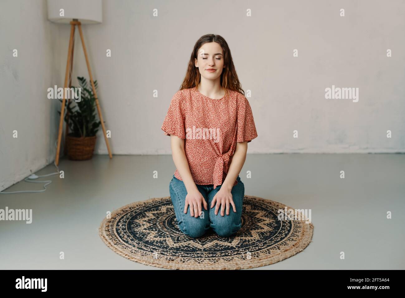 Young woman kneeling on a round mat at home meditating with a serene expression and closed eyes in a health and wellbeing concept with copyspace Stock Photo