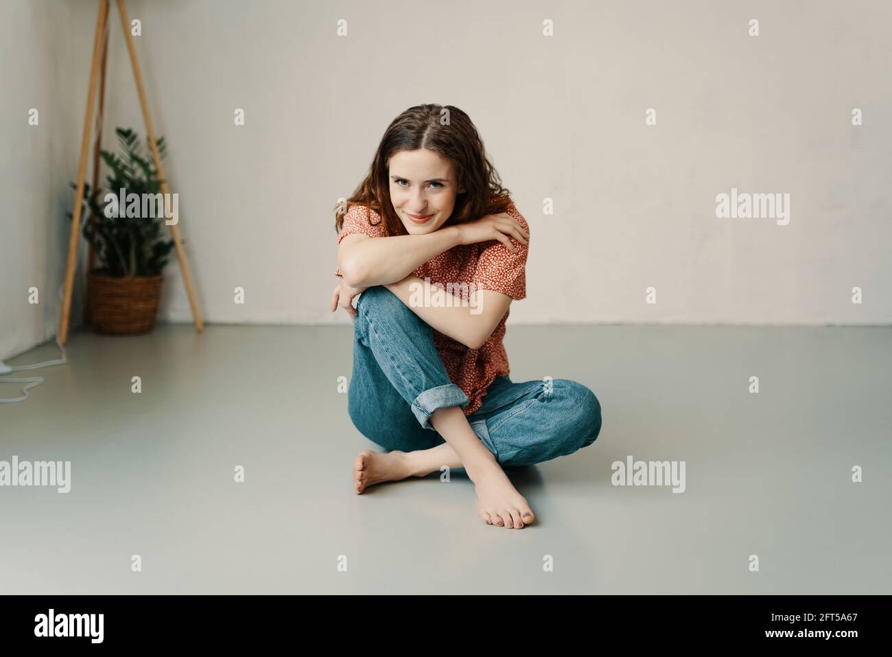 Pretty yung redhead woman relaxing barefoot on the floor with chin on hands looking at the camera with a sweet friendly smile and copyspace Stock Photo