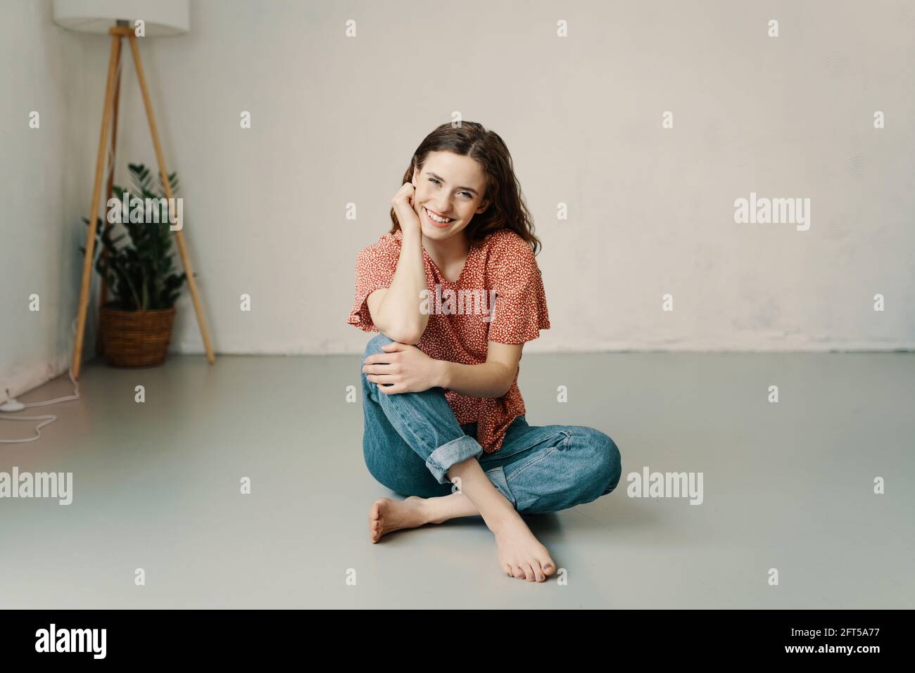 Happy young woman with a lovely beaming smile relaxing barefoot on the floor with chin on hand grinning at the camera with copyspace Stock Photo