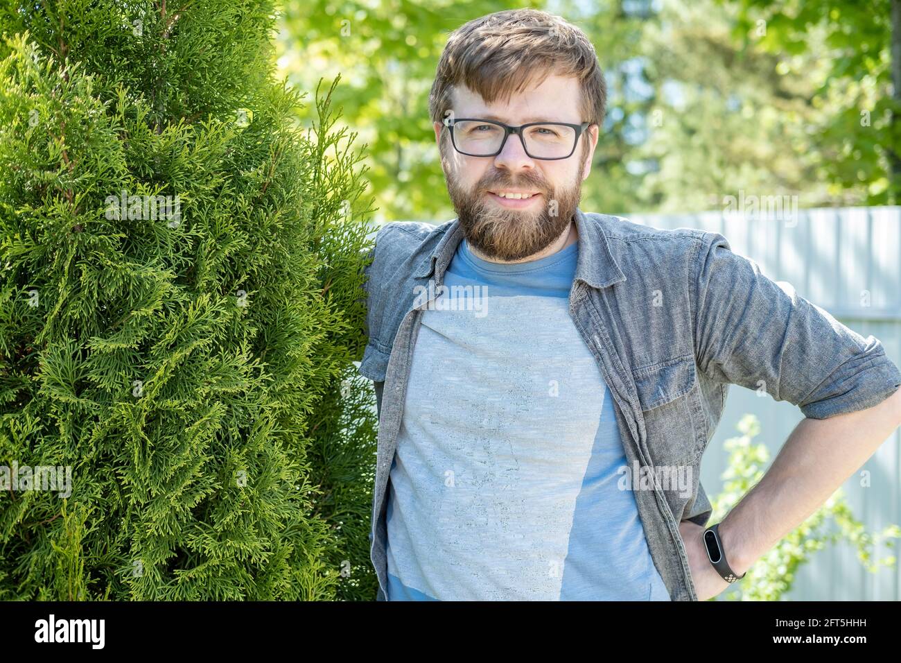 Satisfied male gardener hugs the thuja he raised and smiles sweetly in the garden on a summer day. Stock Photo