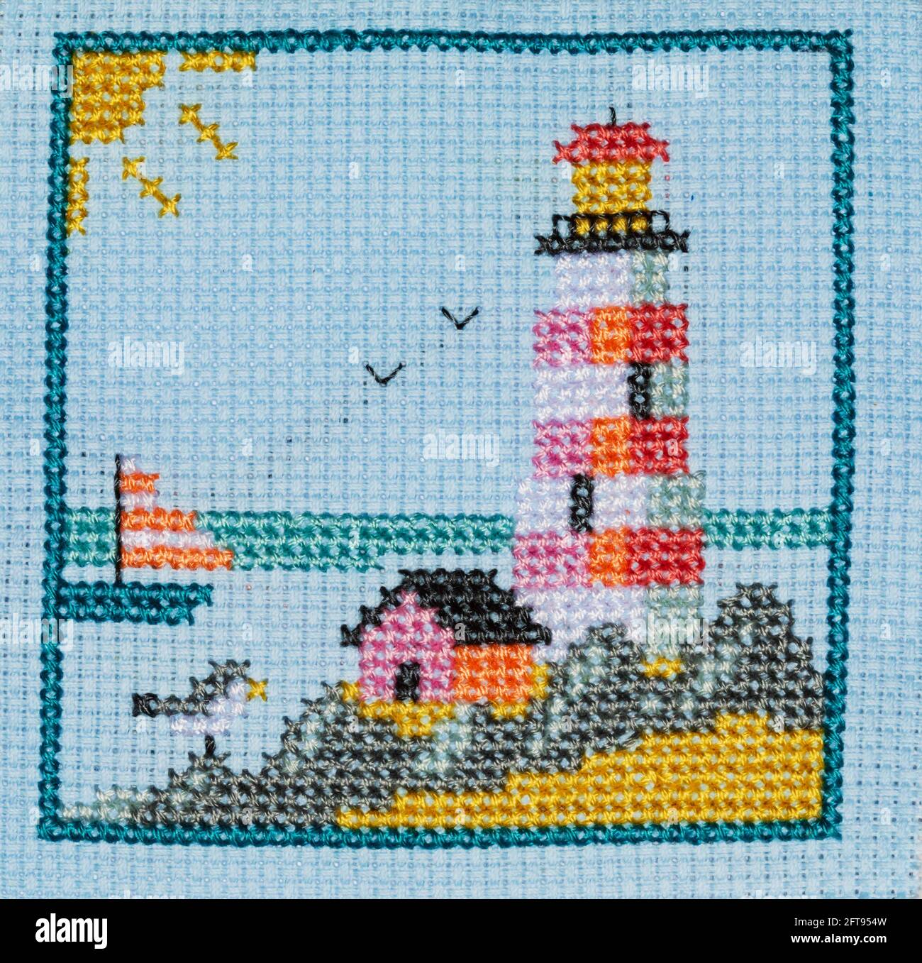 Embroidered needlework picture of the seaside with a lighthouse and yacht. Stock Photo