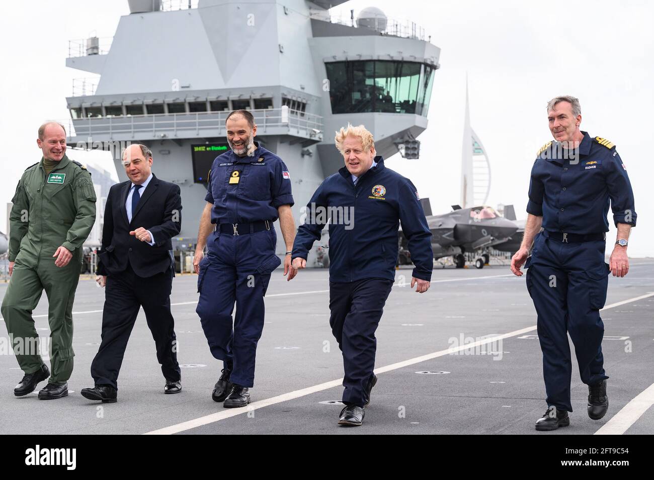 (Left to right) Air Chief Marshal Sir Mike Wigston, Defence Secretary Ben Wallace, Commodore Steve Moorhouse, Prime Minister Boris Johnson, and First Sea Lord Admiral Tony Radakin face strong winds as they walk on the flight deck, during a visit aboard HMS Queen Elizabeth in Portsmouth ahead of its first operational deployment to the Far East. Picture date: Friday May 21, 2021. Stock Photo