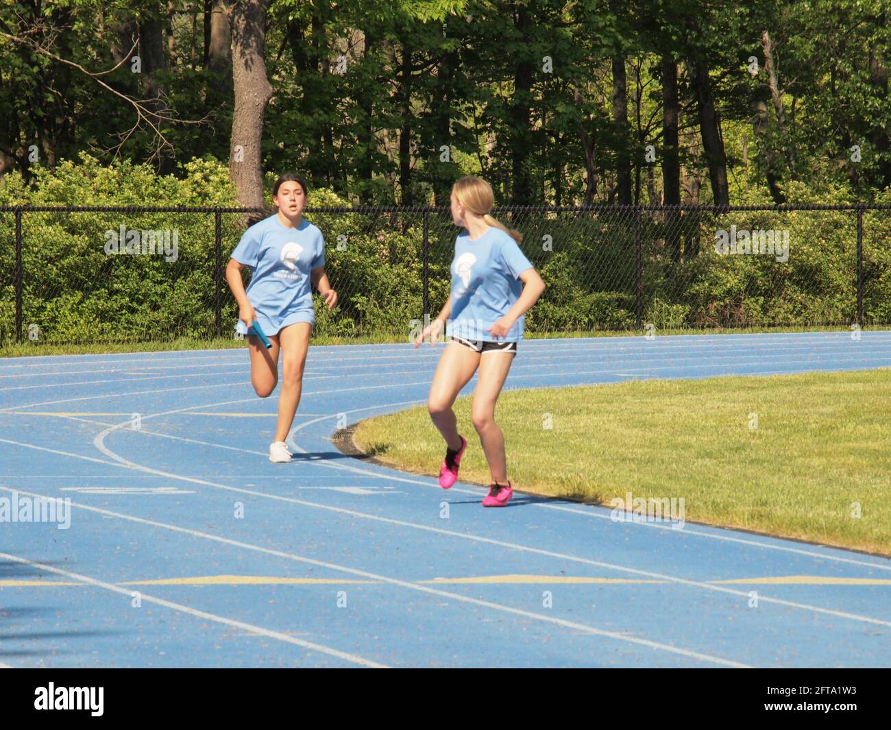Middle school track meet with relay race hand-off and sprinting girl at the finish line. Stock Photo
