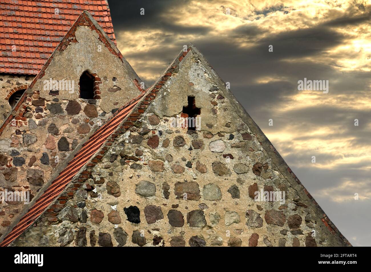 Upper part of pointed roofs of abandoned old village church in Germany, with dramatic clouds in sky Stock Photo
