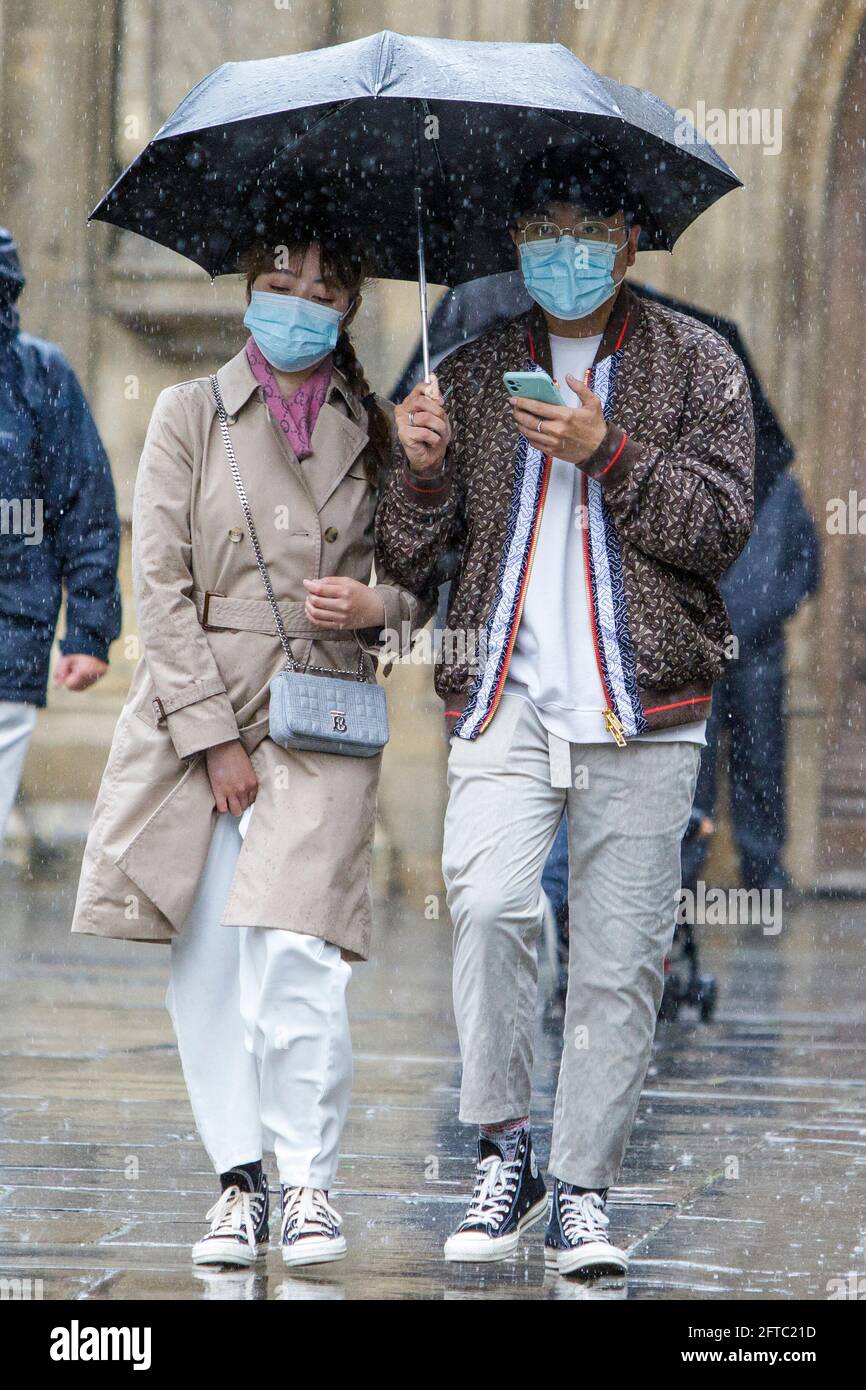 Bath, Somerset, UK. 21st May, 2021. A man and a woman sheltering under an umbrella are pictured outside Bath Abbey as heavy rain showers make their way across the UK.  Credit: Lynchpics/Alamy Live News Stock Photo
