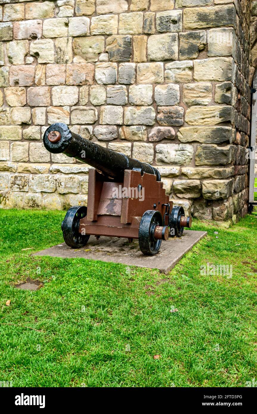 A nine-pounder cannon from HMS George, which sunk in August 1732, stands on a wooden gun carriage in front of a tower of Etal Castle gatehouse Stock Photo