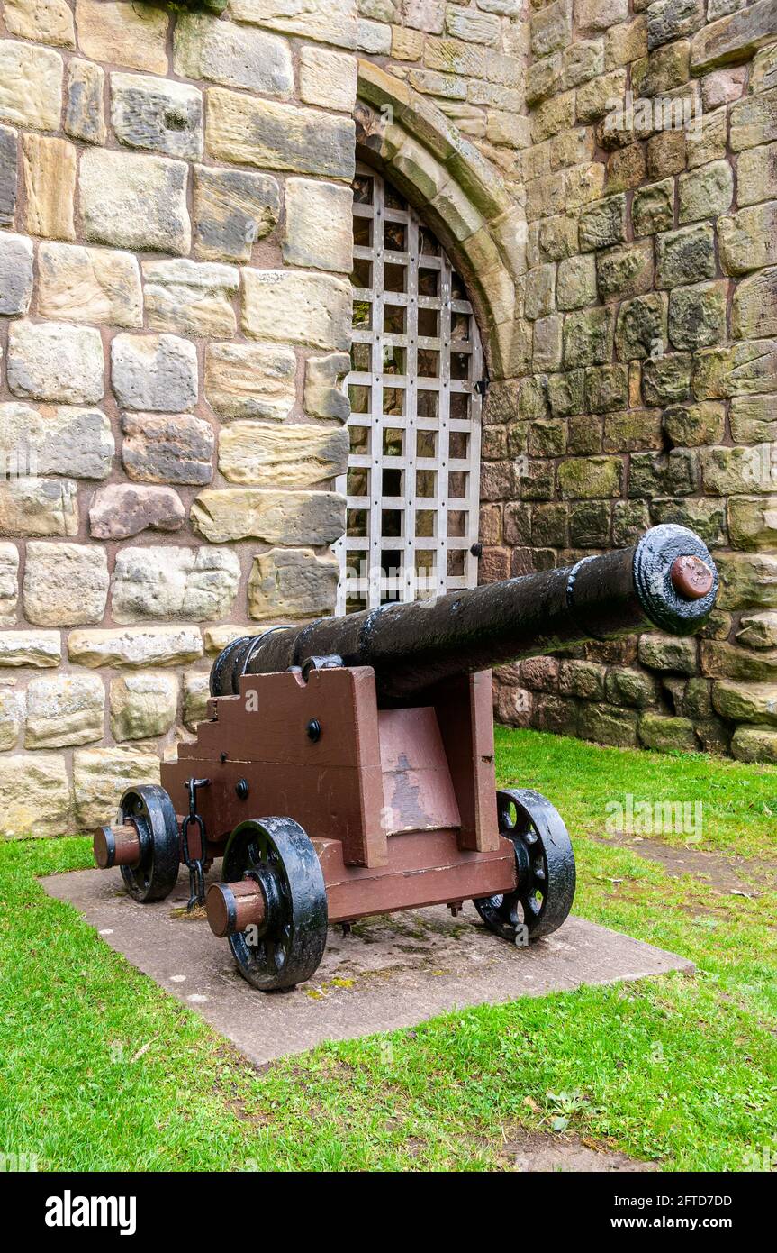 A nine-pounder cannon from HMS George, which sunk in August 1732, stands on a wooden gun carriage in front of a tower of Etal Castle gatehouse Stock Photo
