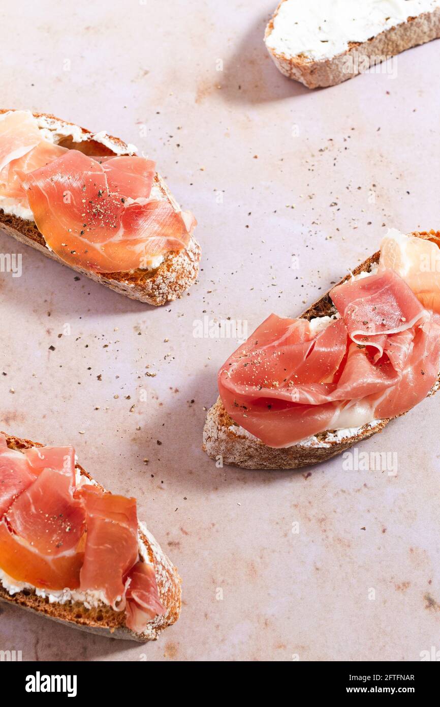 Baguette slices topped with whipped cream cheese, Serrano ham and cracked pepper. Stock Photo