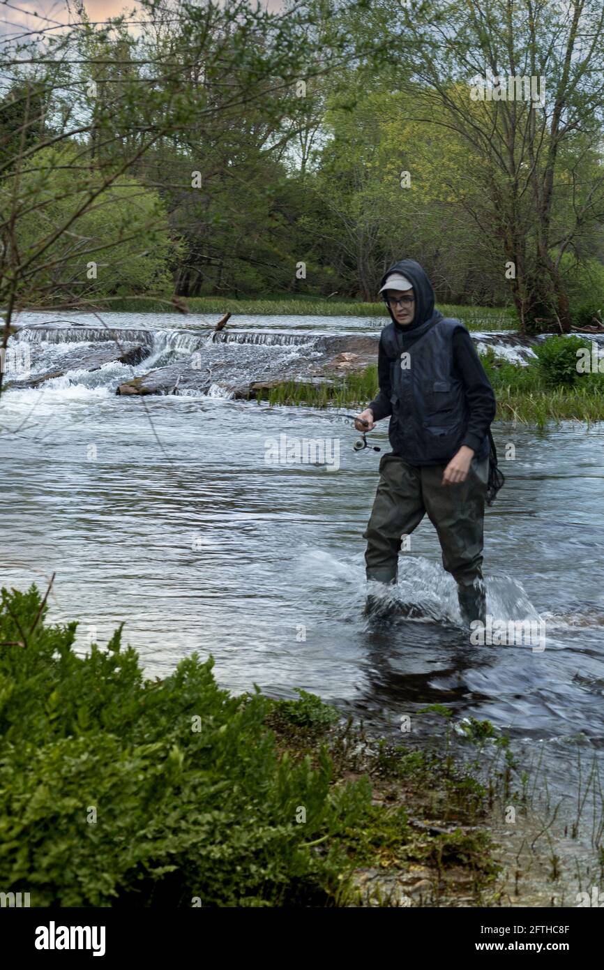 fisherman in vest, cap and hooded sweatshirt wading in the river