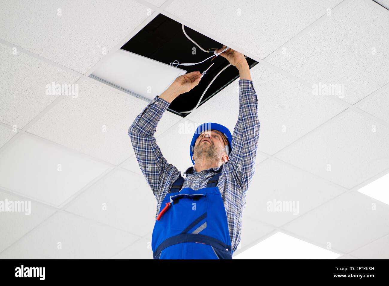Electrician Installing LED Ceiling Light In Office Stock Photo