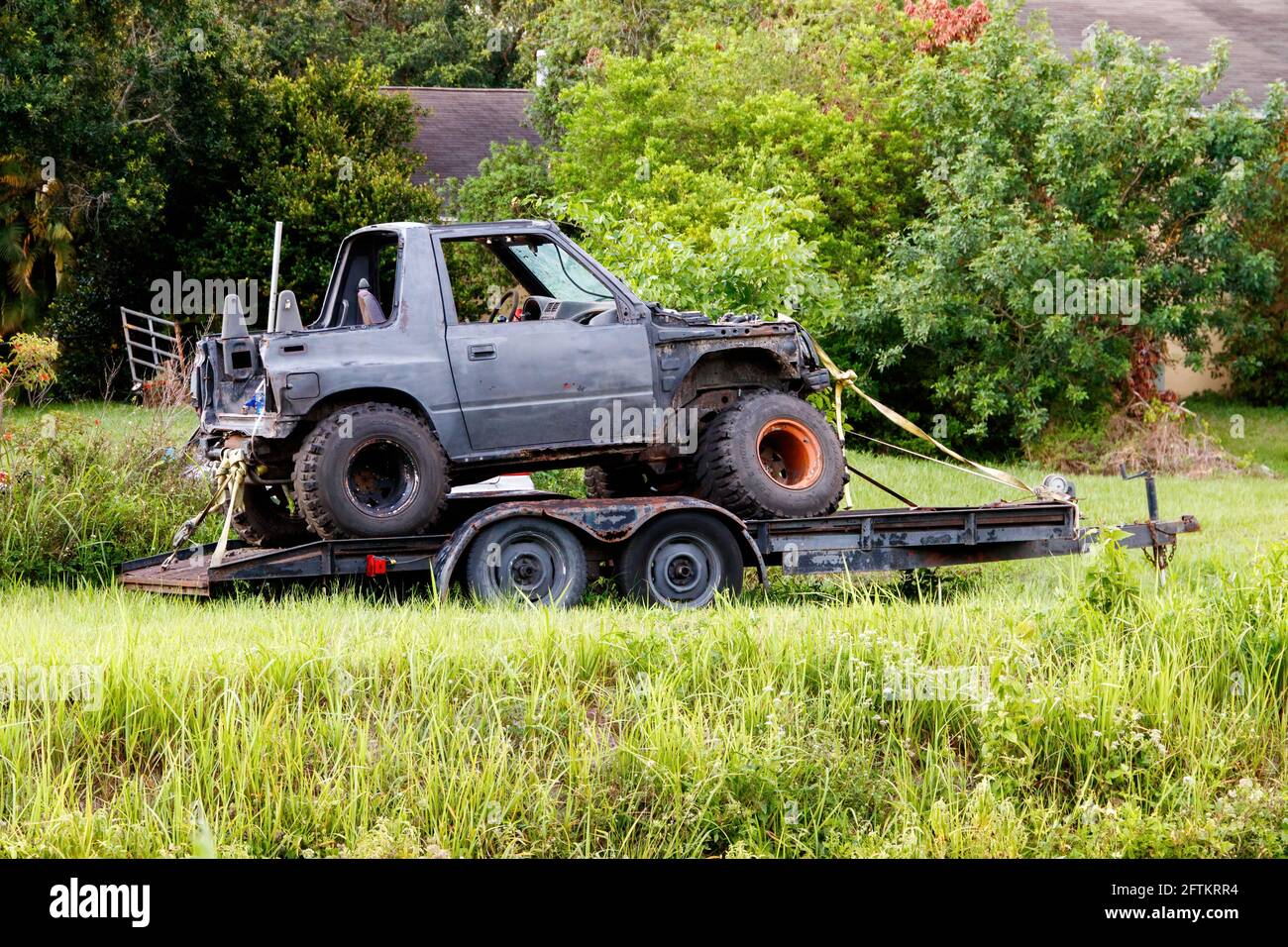 Loxahatchee, Florida, USA - May 16, 2021: Four wheel drive type truck with oversized jumbo dirt tires on a motor boat trailer rusted, missing fenders. Stock Photo