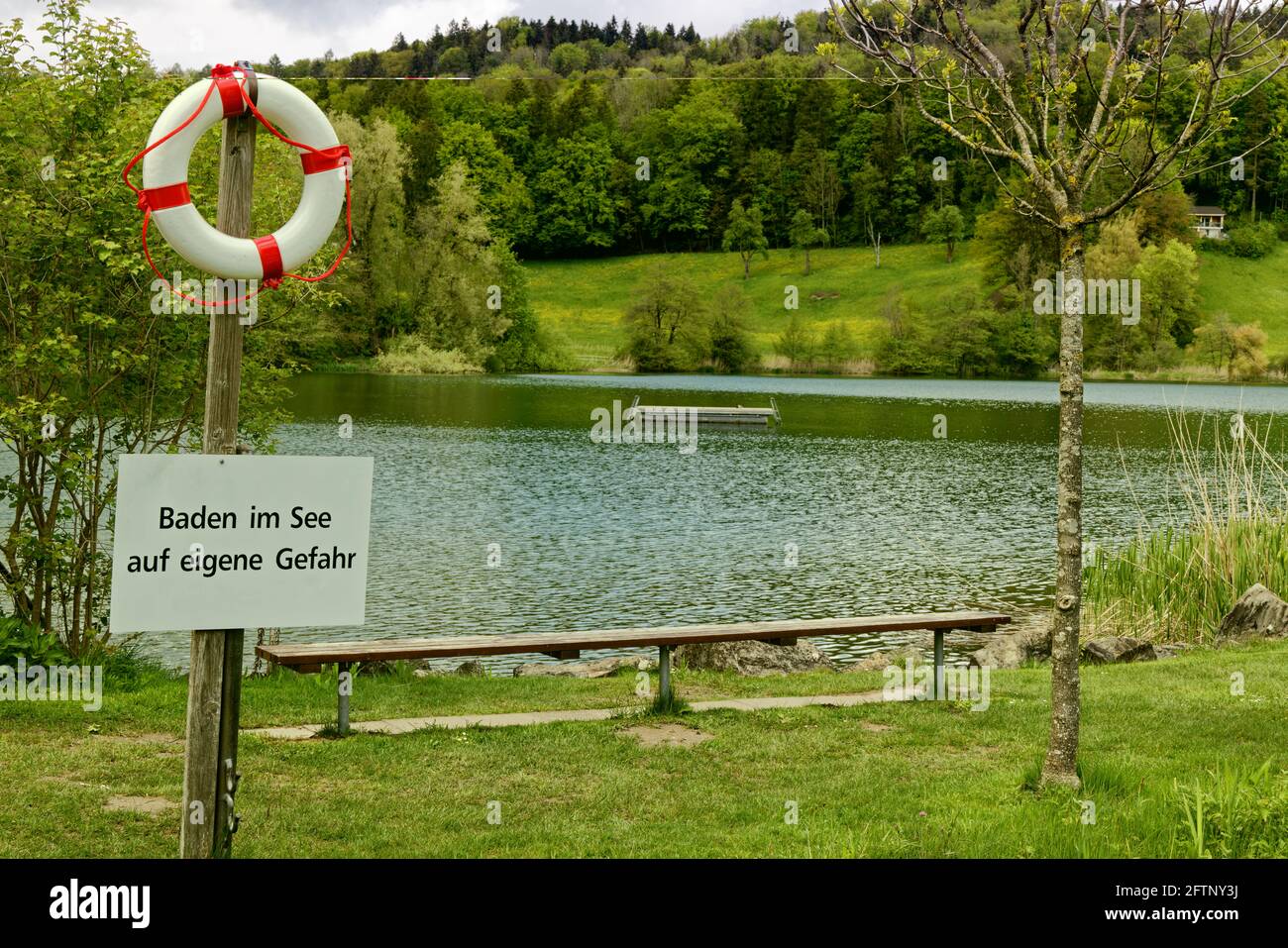lake outdoor pool with swimming platform in green landscape with notice sign in german, german text translation: swim in the lake at your own risk at Stock Photo