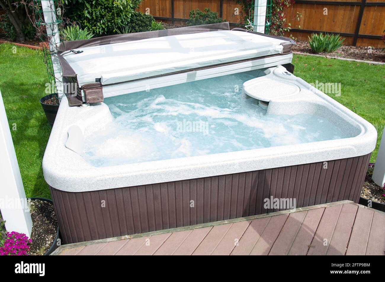 Hot tub in back yard with water bubbling and the lid half off, ready to