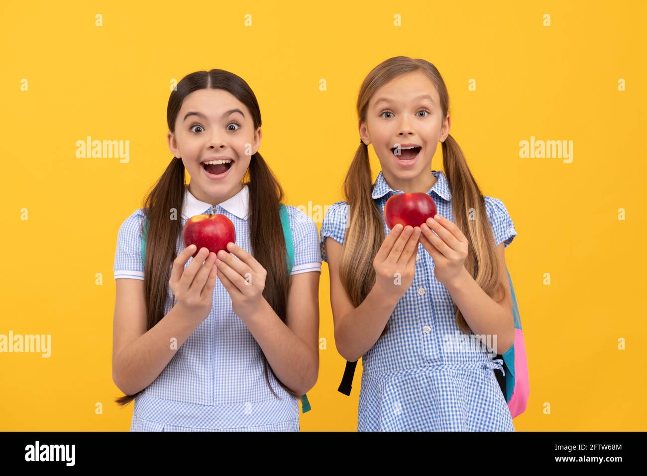 Surprised school age kis hold tasty organic vitamin apples yellow background, healthy food Stock Photo