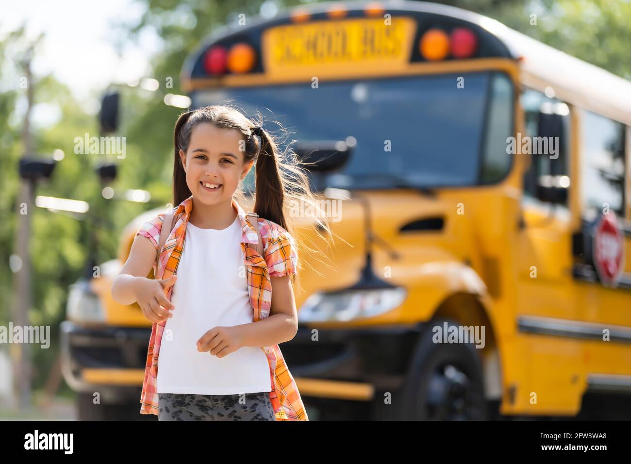Little girl standing by a big school bus door with her backpack. Stock Photo