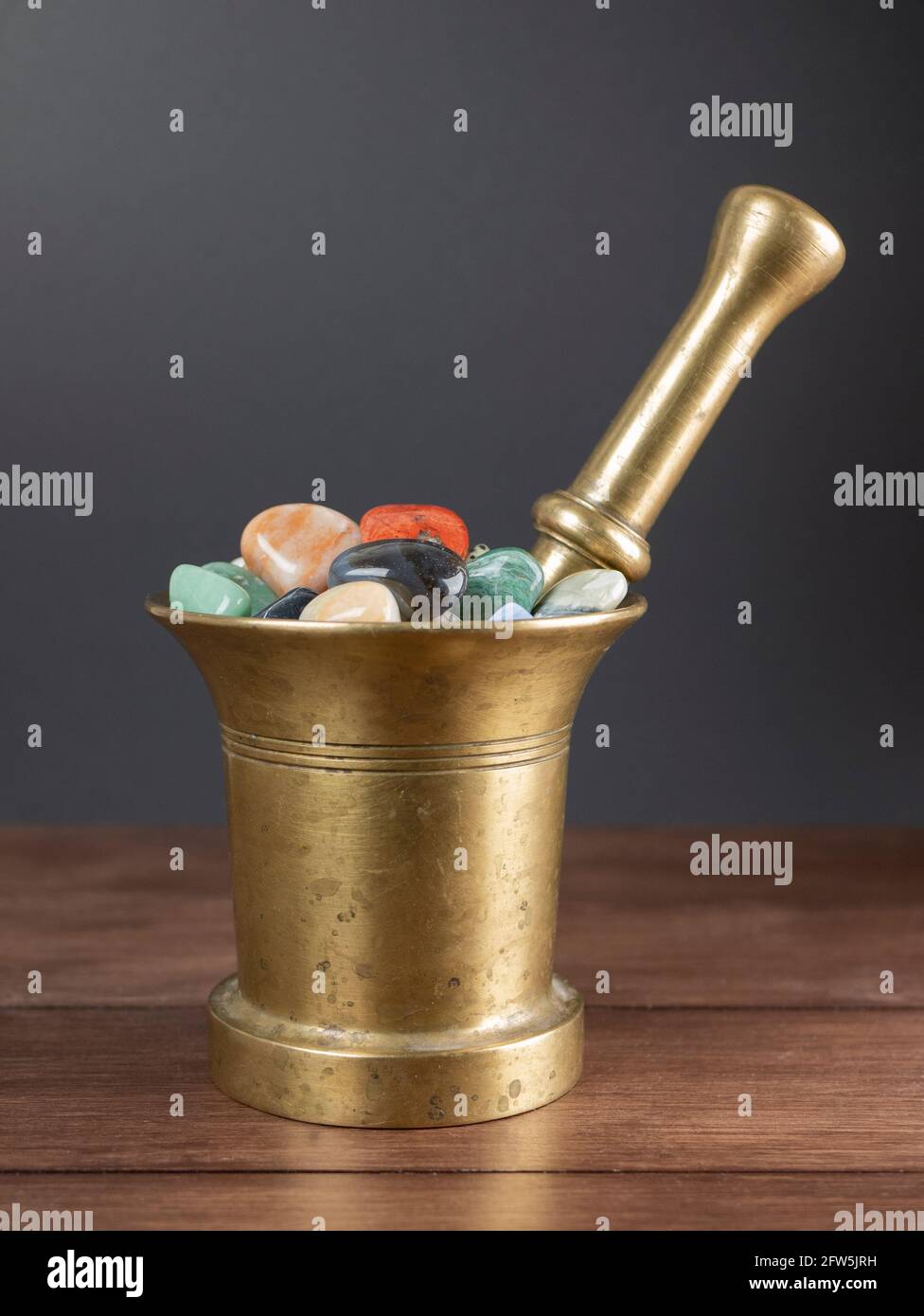 Multicolored stones and minerals in the old mortar with pestle. Concept of lithotherapy, ancient medicine and alchemy Stock Photo