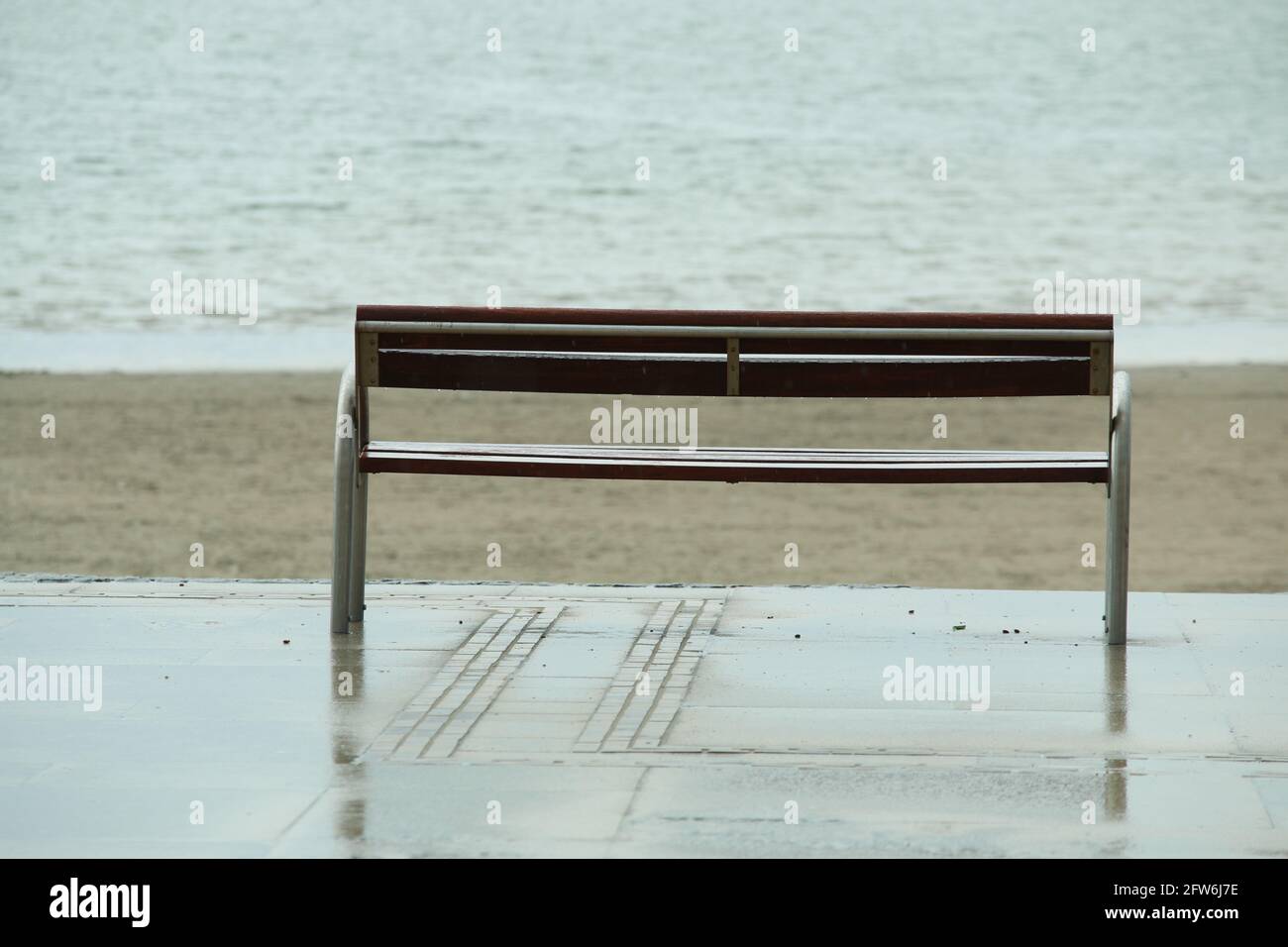 Wooden bench in front of the beach and the ocean on a rainy day Stock Photo