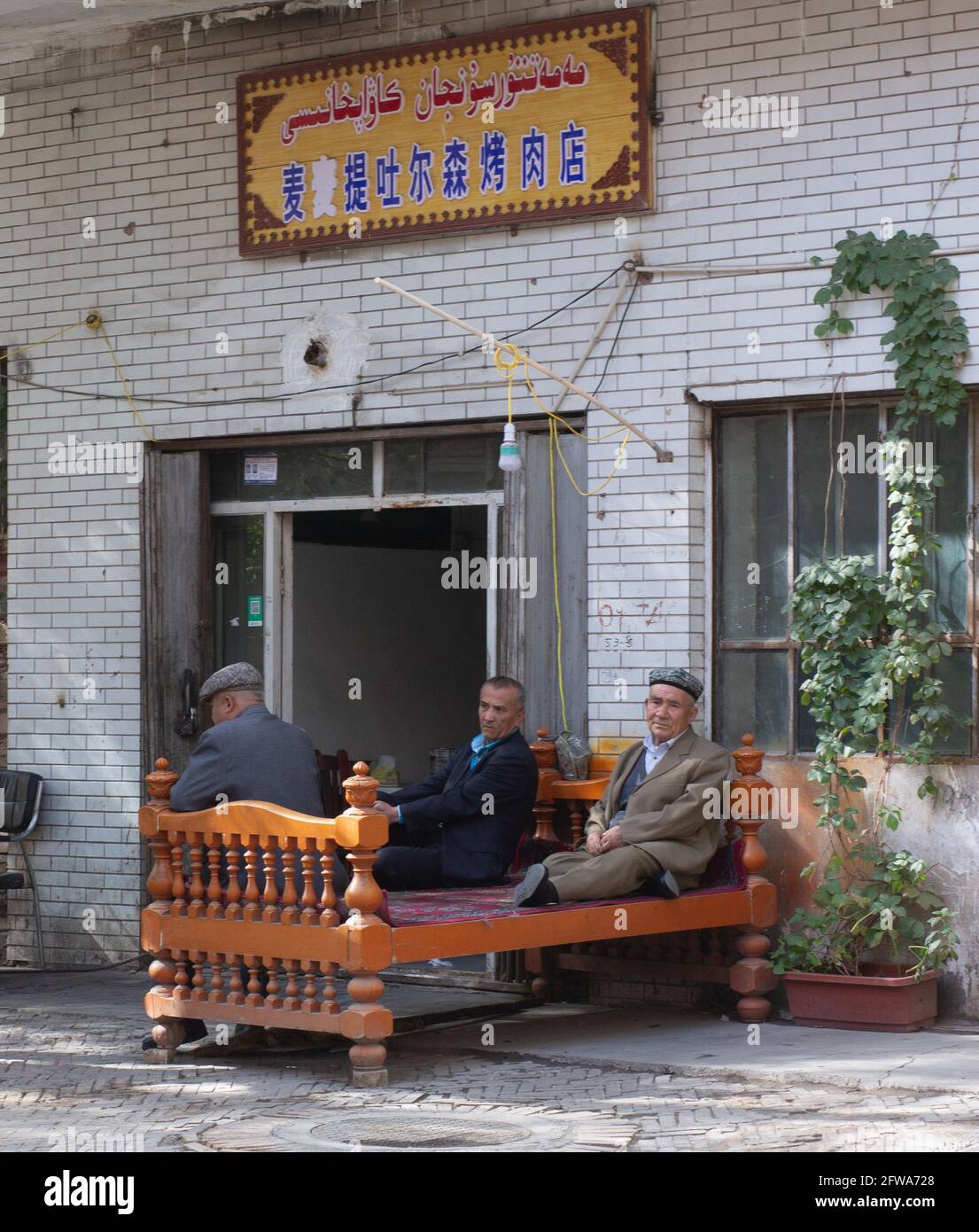 Three adult men sitting on a bed outside the tent Kashgar, Xinkiang, Popular Republic of China, 2019 Stock Photo