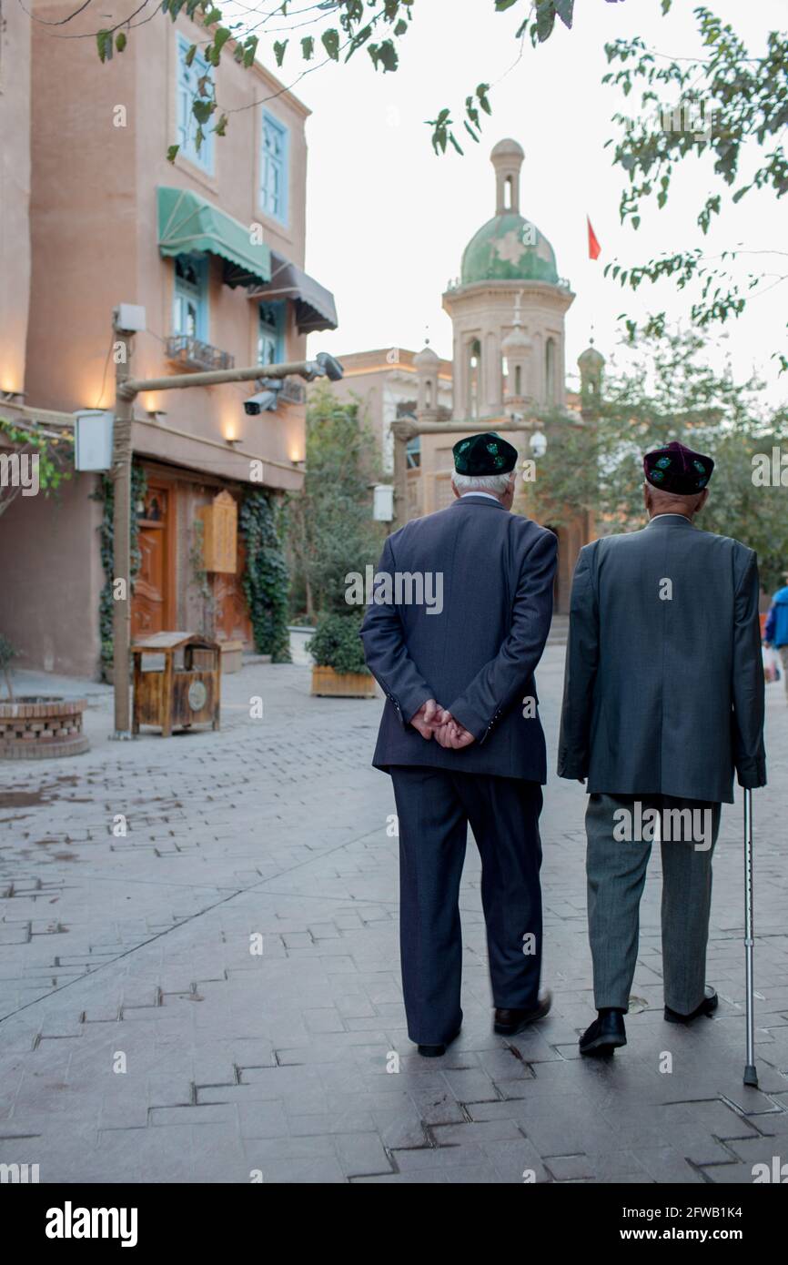 Two elder man wit traditional Uyhgur hat walking near the  mosque. Kashgar, Xinkiang, Popular Republic of China, 2019 Stock Photo
