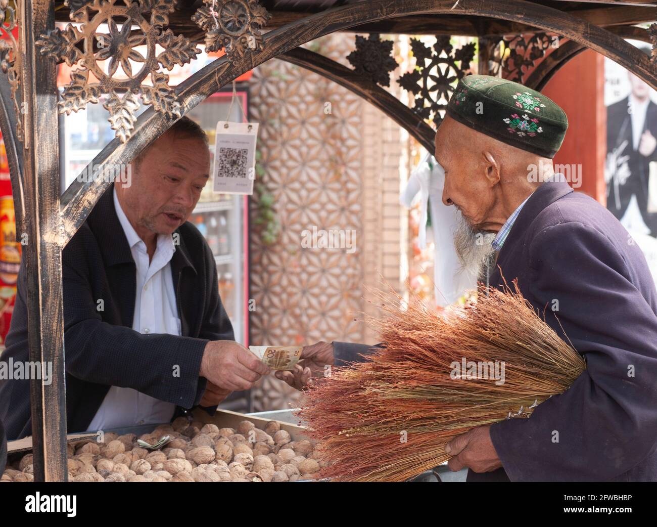 A street vendor of brooms buying nuts. Kashgar, Xinkiang, Popular Republic of China, 2019 Stock Photo