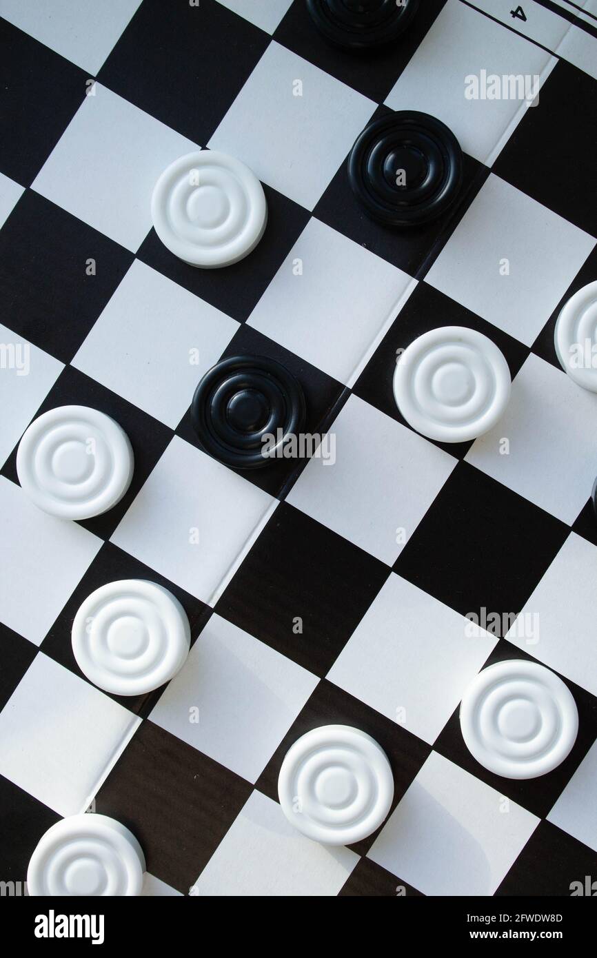 Board game of checkers. Black and white chips for the game. Chess field. Checkers move close-up. Checker in hand. Stock Photo