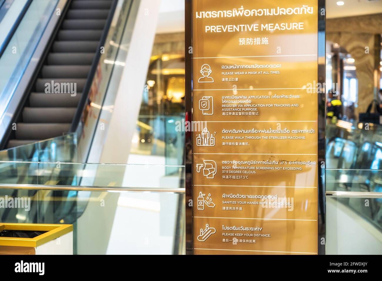 Covid-19 pandemic, new normal Concept, Preventive Measure Text with Thai and Chinese Language on the Billboard before escalator in department store Stock Photo