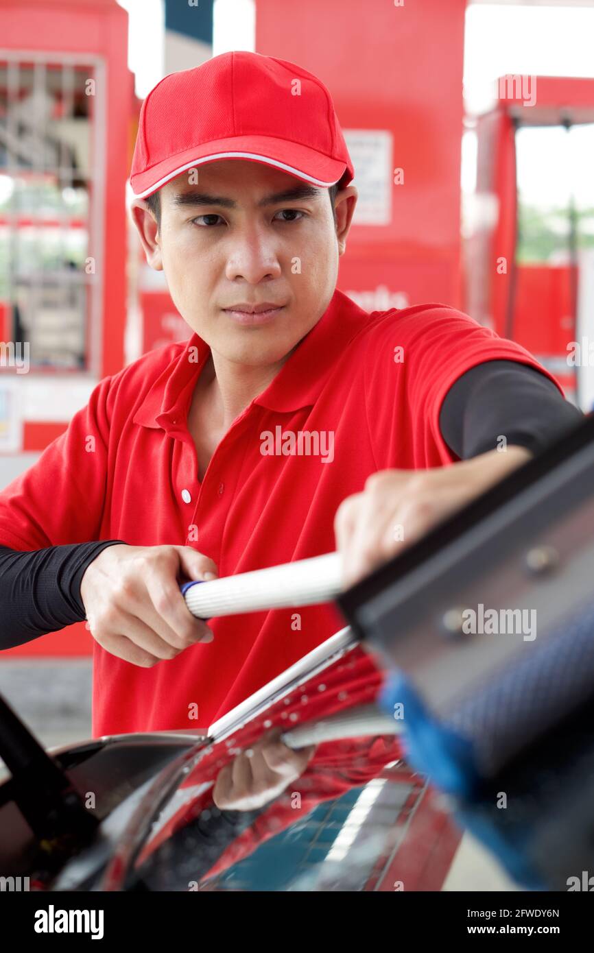 Asian gas station worker in red uniform cleaning the car windshield