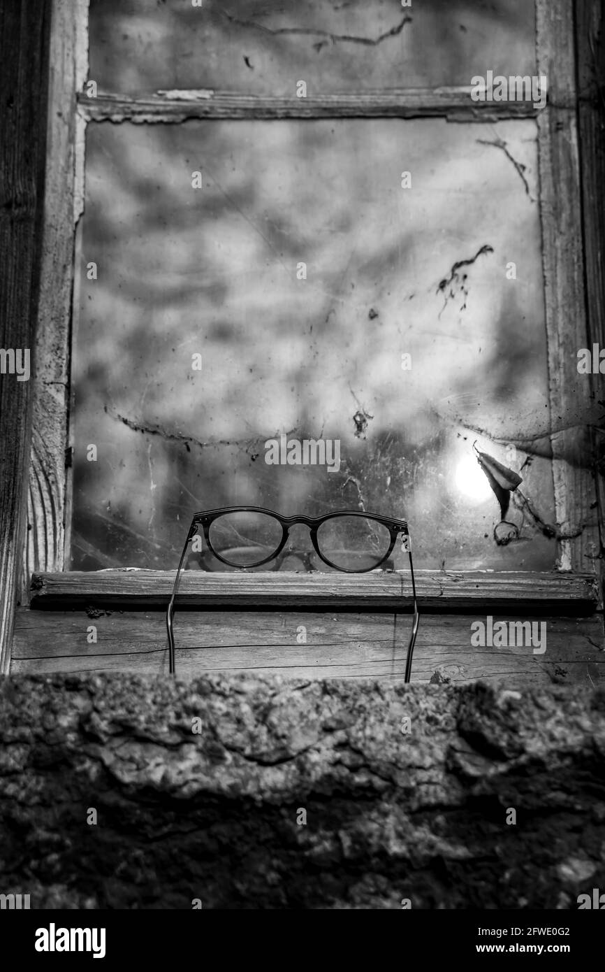 Vintage reading glasses lie on window sill against the window reflection of clouds - Black and White Stock Photo