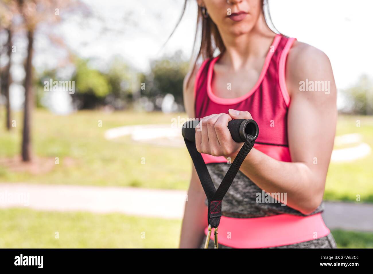 hands of a woman using resistance bands. She is unrecognizable. In a green park. Selective focus in hands Stock Photo