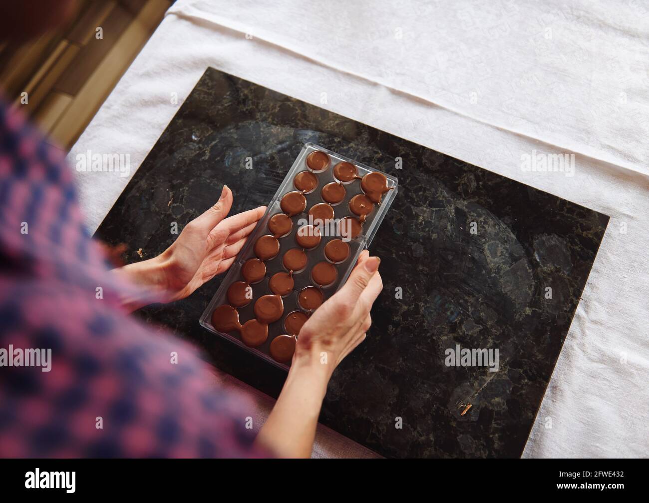Closeup of female hands holding chocolate molds full of liquid heated