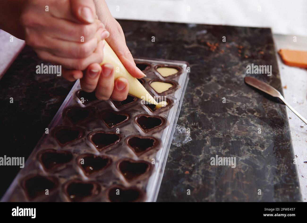 Closeup of squeezing filling of salted caramel cream from confectionery bag  into candy molds for preparing handmade chocolate pralines Stock Photo -  Alamy