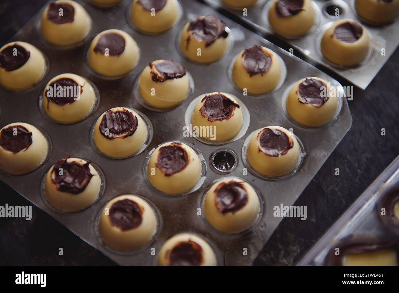 Closeup of manufacturing chocolate truffles. Spherical molds of white