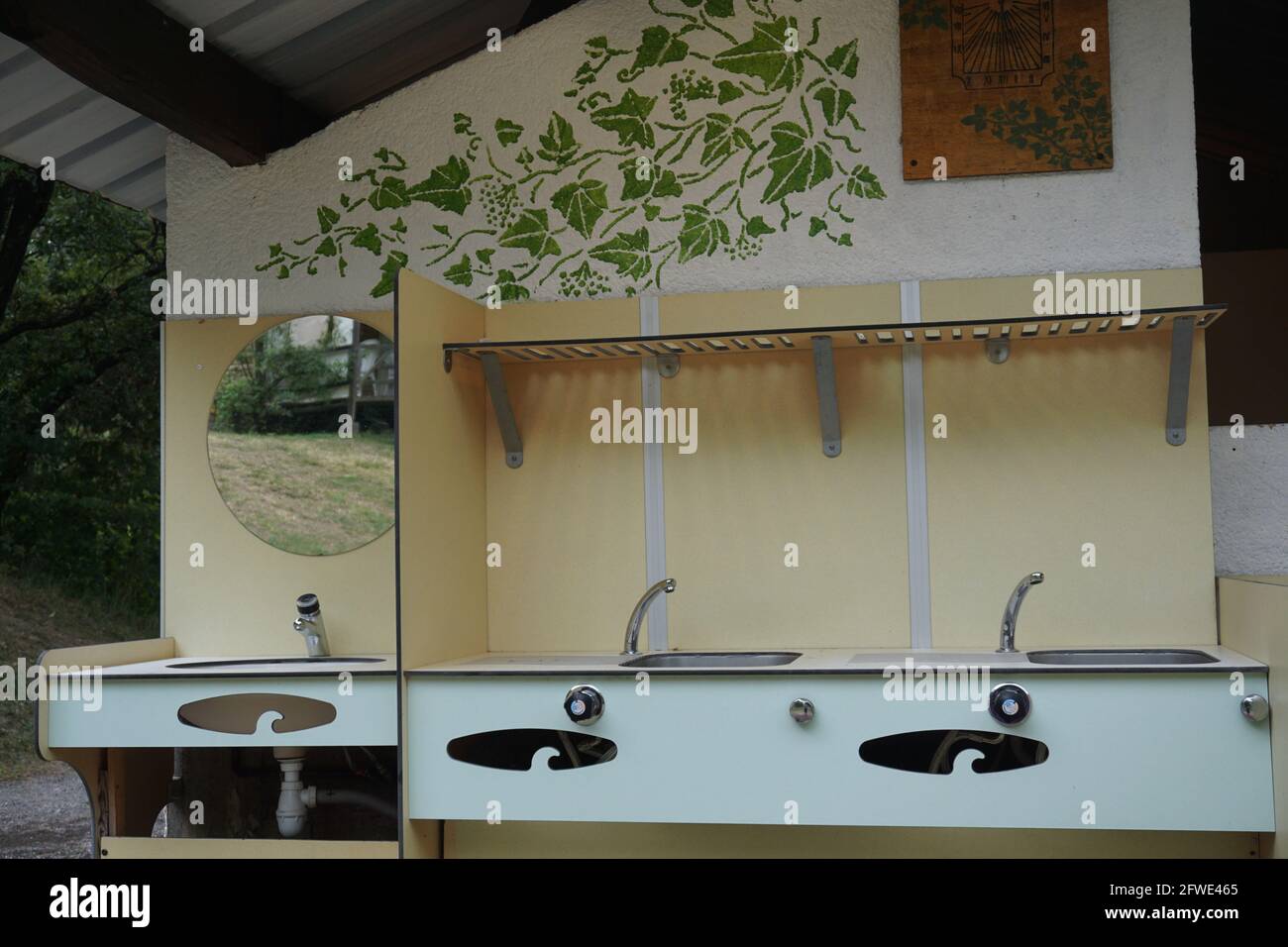 outdoor bathroom and sinks with a painting of leaves on the wall at a camping Stock Photo