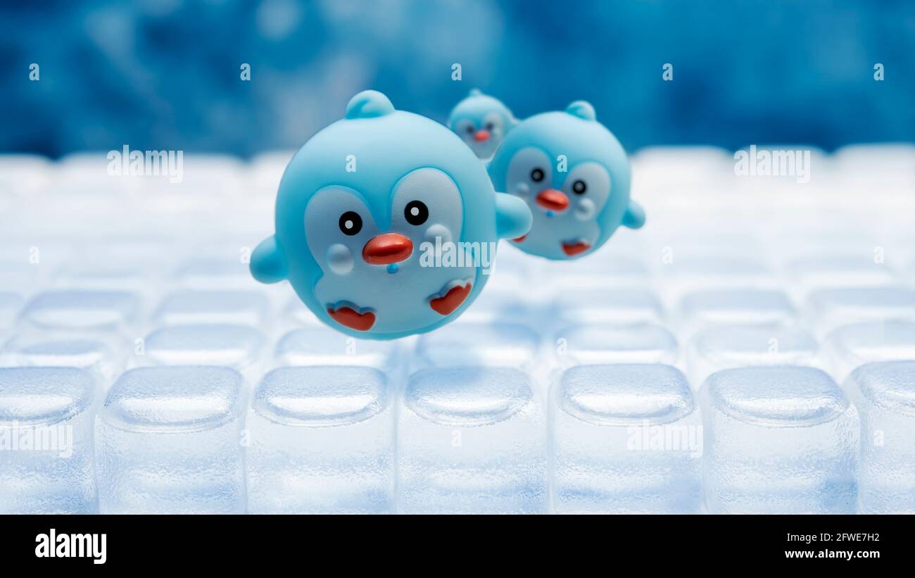 Penguin toy sliding over ice blocks ,selective focus and blue background. Stock Photo