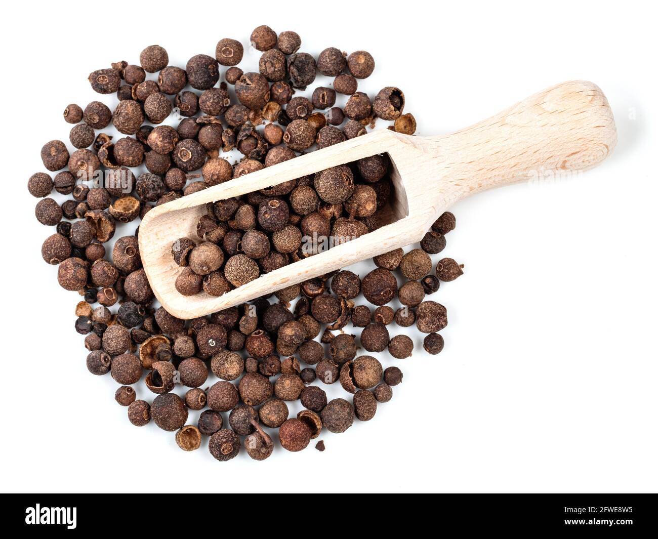 top view of wooden scoop on pile of allspice (jamaica pepper) on white