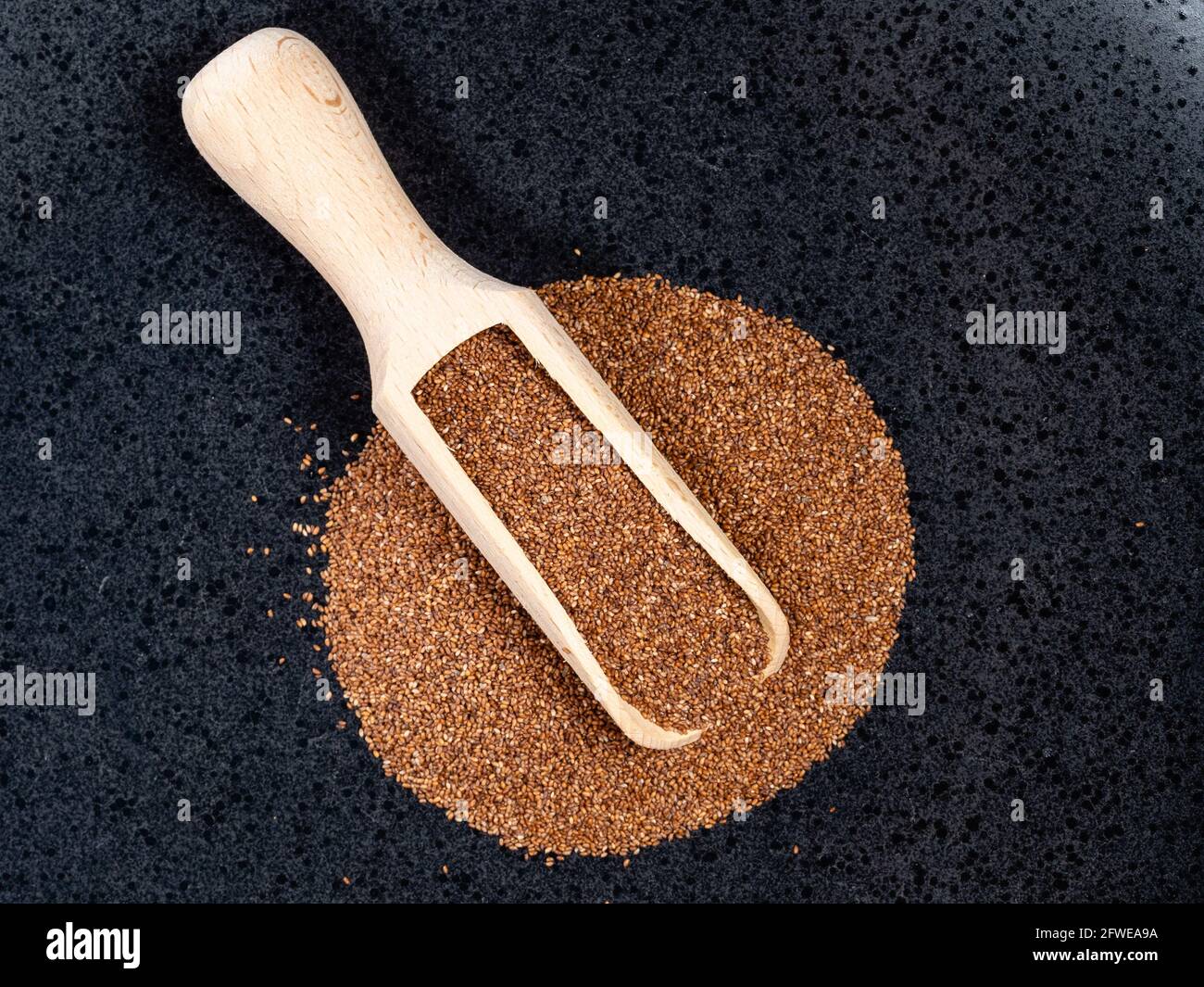 top view of wood scoop on pile of wholegrain teff seeds on black plate Stock Photo