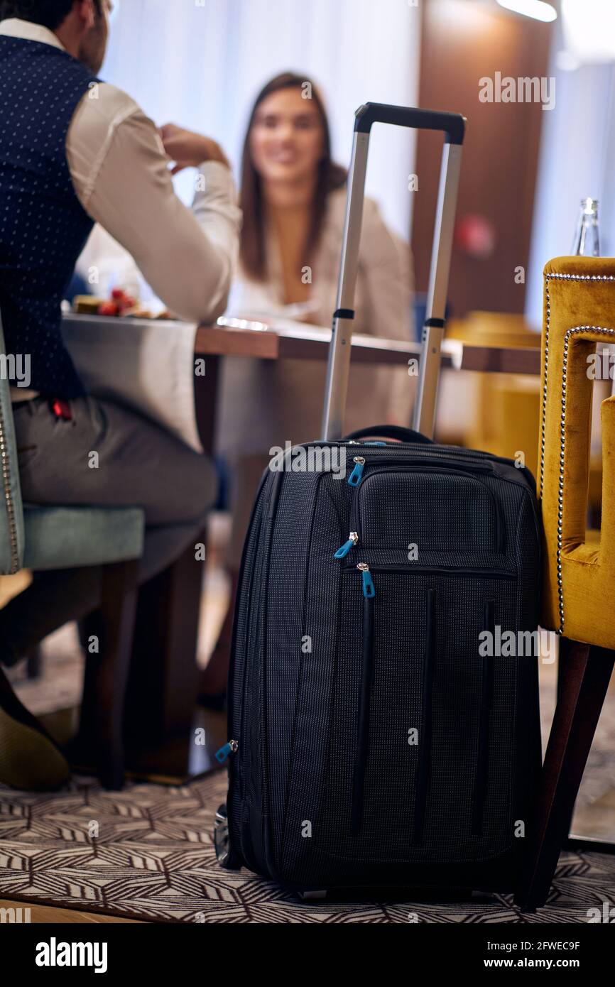 focus on suitcase on wheels in hotel with people in the background having lunch Stock Photo