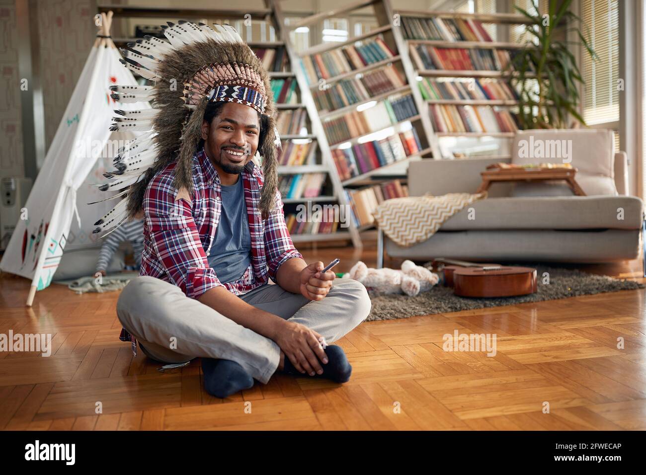 A young man with an indian headdress sitting on the floor in a relaxed ...