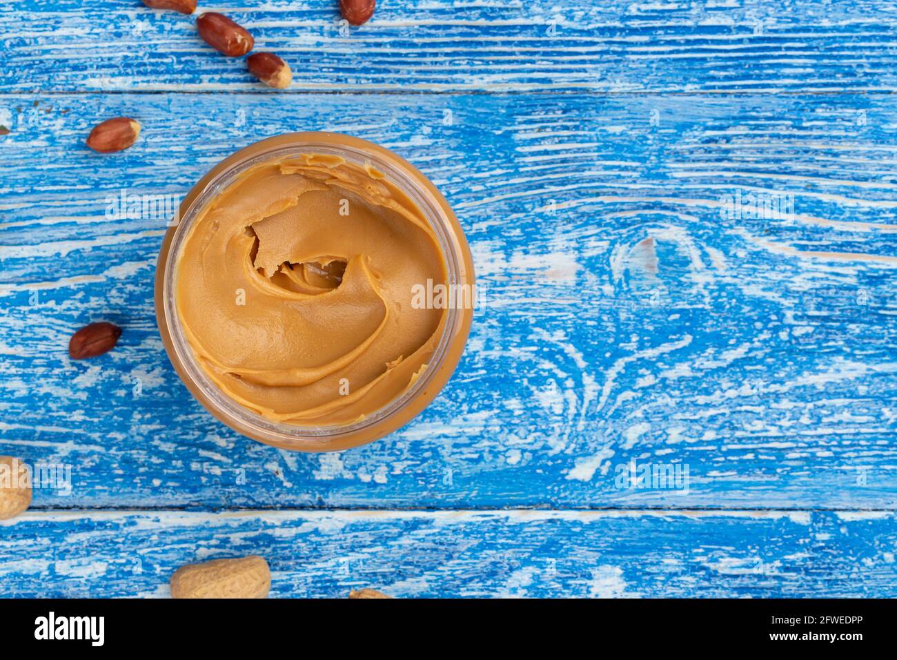Peanut butter in an open jar and peanuts in the skin are scattered on