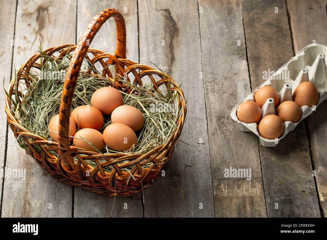 Chicken eggs in a hay basket and egg tray, on a wooden table ...
