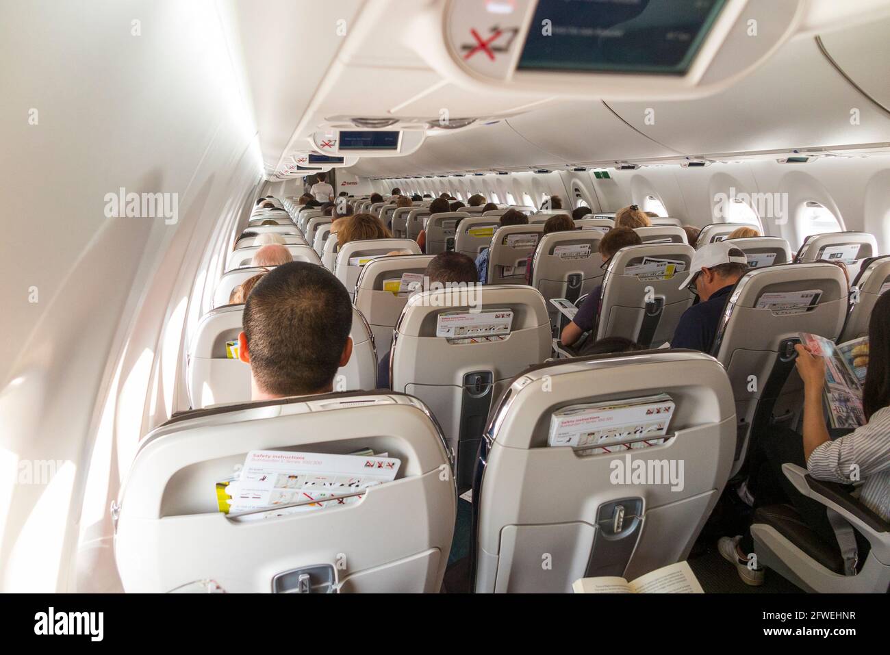 The cabin aisle with seat backs and passengers seen from behind on a Bombardier C series plane / aeroplane / airplane (an aircraft now marketed as an Airbus A220). (100) Stock Photo