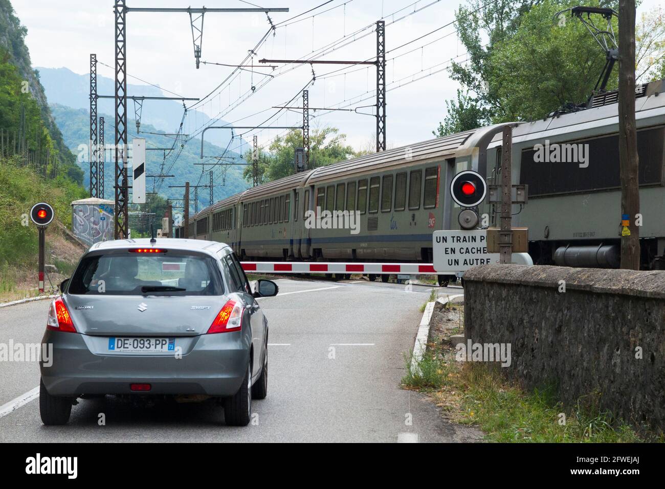Fast train passing & a red traffic signal shows / flashing light / warning lights for a halted car at a French railways rail railway automatic level crossing in France. (100) Stock Photo