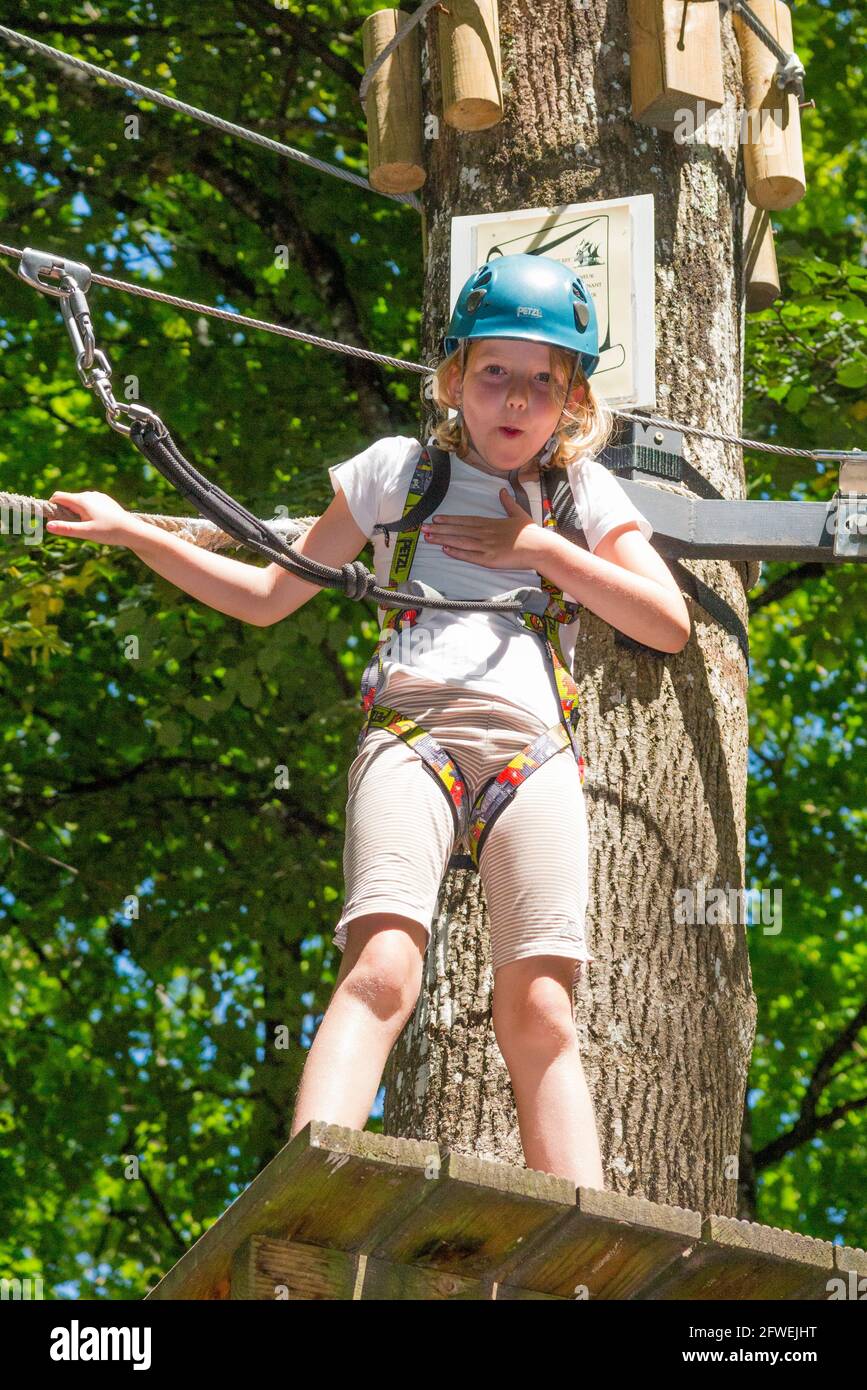 Young girl girls child kid expresses shock, surprise, mild fright, whilst on a children obstacle course activity trail high in woodland forest tree, at an adventure park in France during the summer. Rather like a Go Ape experience. (100) Stock Photo